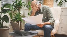 An older man puts his head in his hand while looking at paperwork.