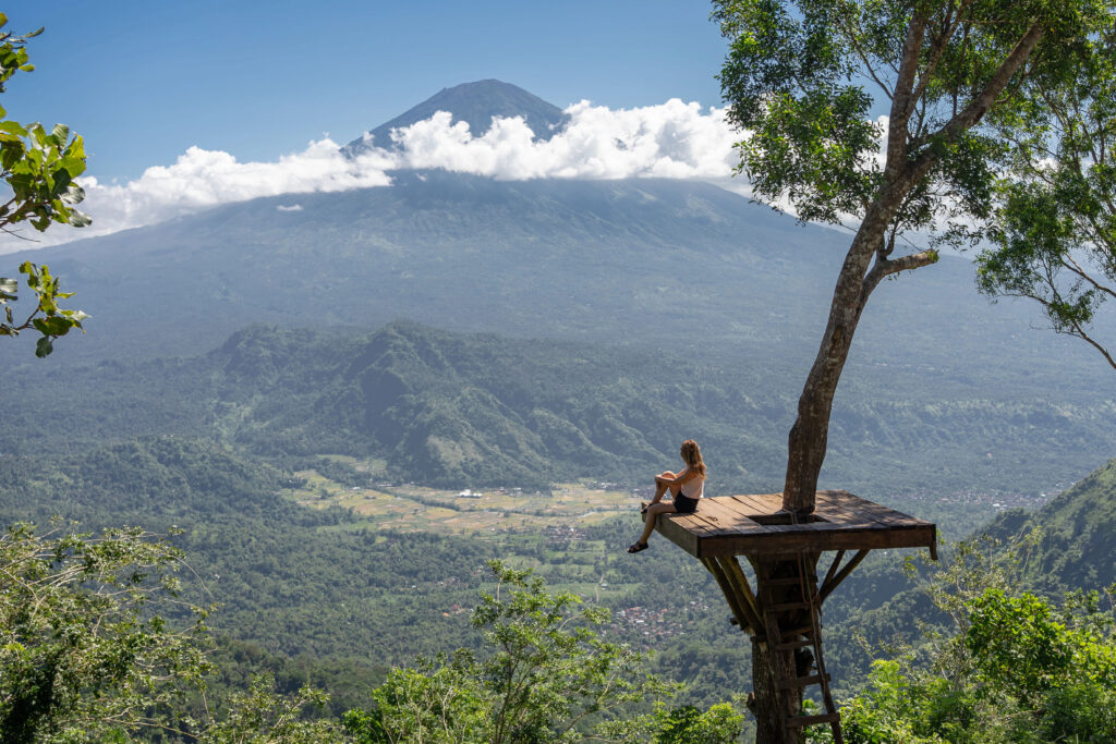 Female tourist looking at the mountains and Agung volcano while standing on photo spot on a tree in Bali, Indonesia