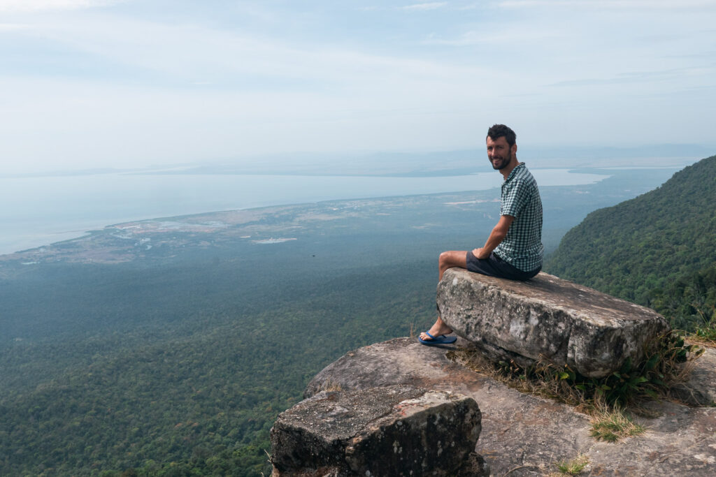 Marek sits on a rock at the edge of a cliff on Bokor Mountain, Cambodia
