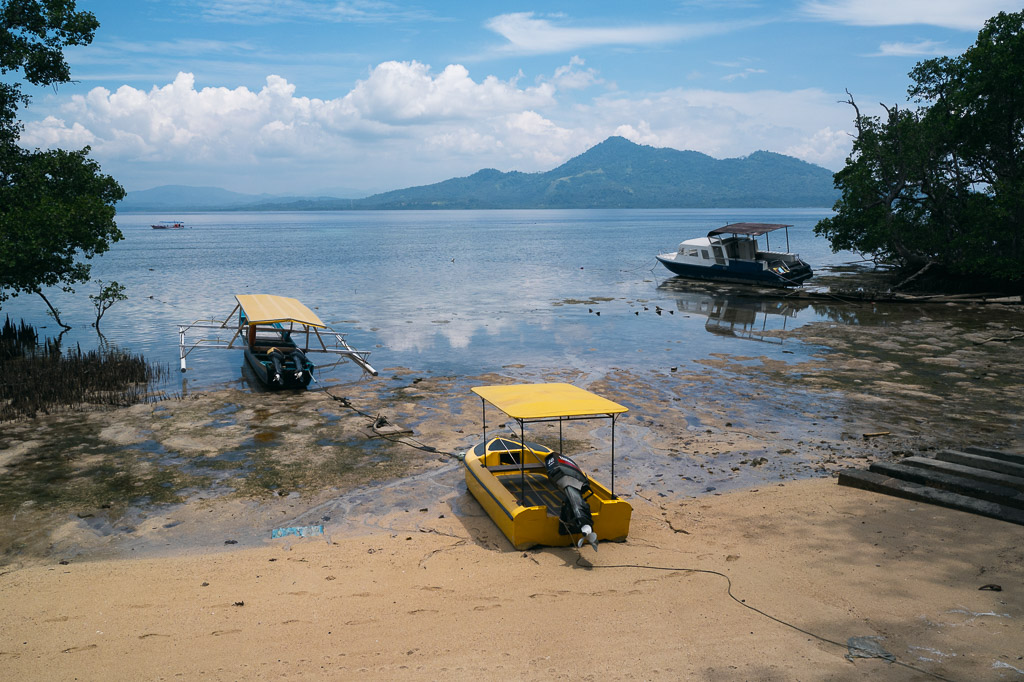 Sandy beach on Bunaken Island with yellow boats and a green mountainous island in the background