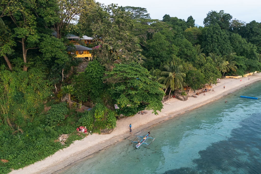 Aerial view of Bunaken coastline with sandy beach, turquoise water, and a boat by the shore
