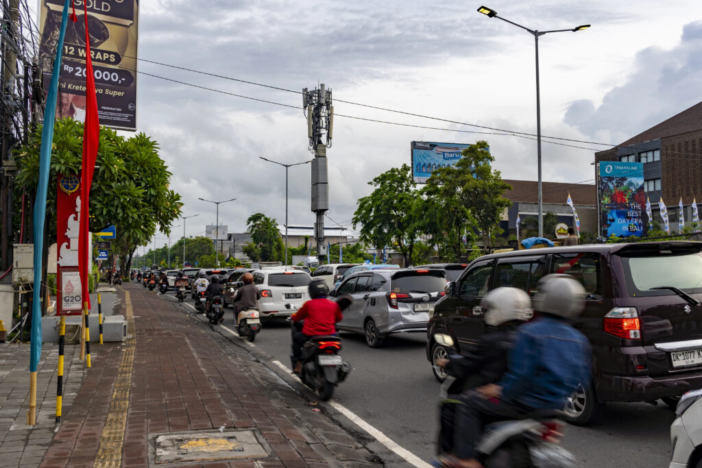 A busy street scene in Bali with many motorbikes and cars lined in traffic
