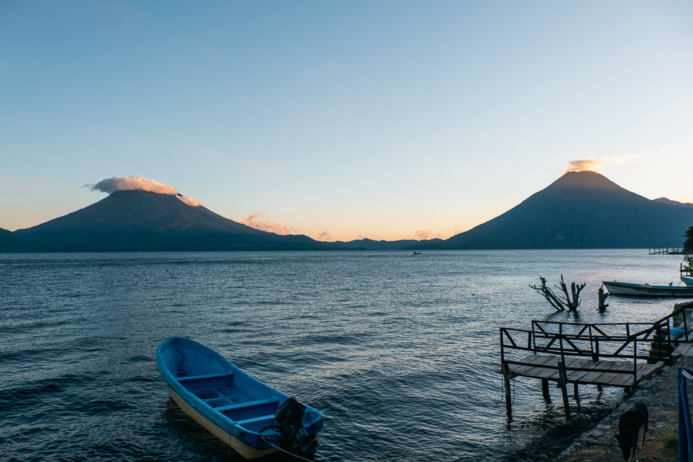 A blue boat floating on Lake Atitlan, Guatemala with two volcanos in the background.