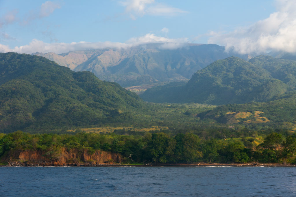 A lush, green mountainous coastline in Flores, Indonesia, viewed from the sea