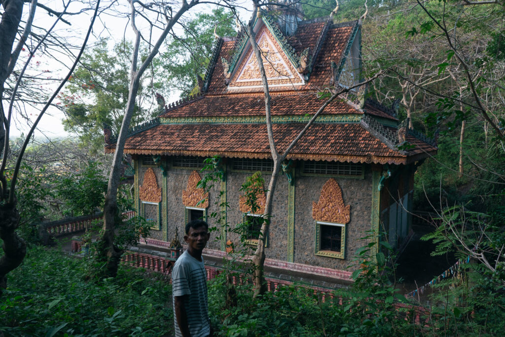 A traditional Cambodian building with a tiered roof and ornate details hidden by trees in Kampot, Cambodia
