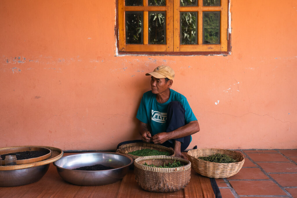 A person sitting on the floor in front of baskets and bowls, against an orange wall in Kampot.