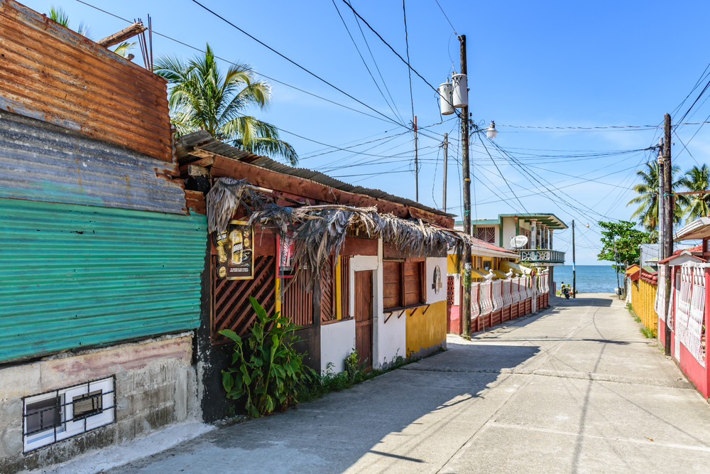 A paved street sandwiched between houses in Livingston, Guatemala with the sea in the background.