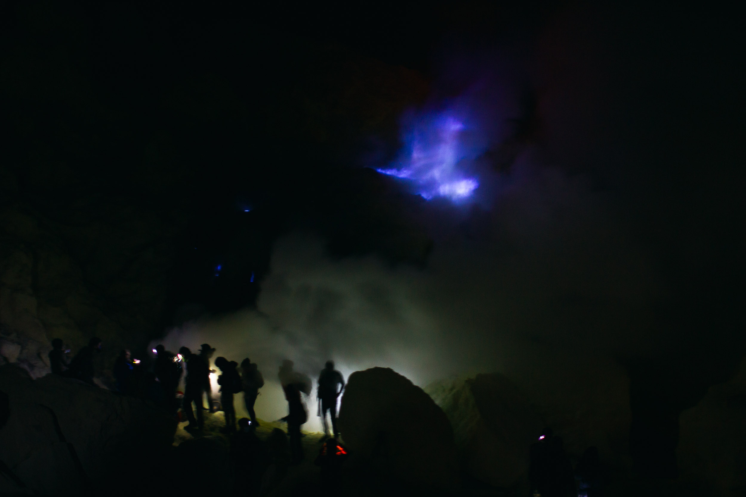 Blue flames at Mount Ijen at night, with smoke and a group of hikers