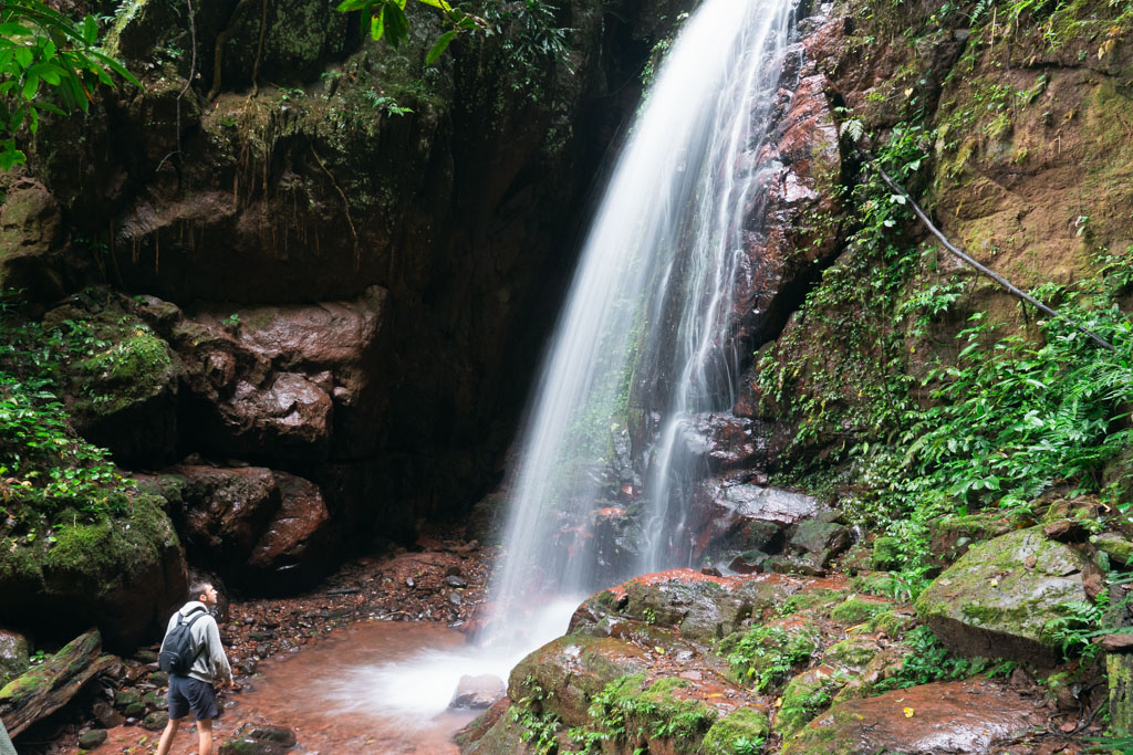 A man standing at the bottom of a waterfall in Laos.