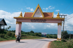 A person riding a motorcycle on a road in Luang Namtha, Laos and an arch in the background.