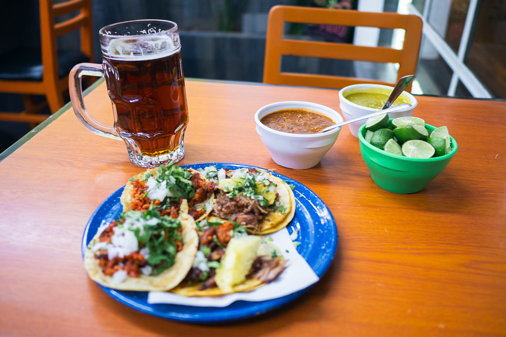 A close-up shot of a blue plate with three Vallarta tacos, mexican food topped with various meats and garnishes in a restaurant in mexico city