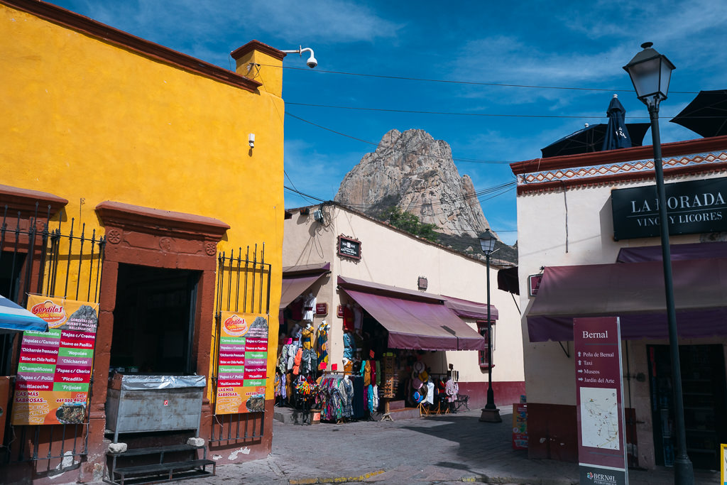 A street scene in Peña de Bernal, Queretaro, Mexico, showing shops and a monolithic rock formation in the background