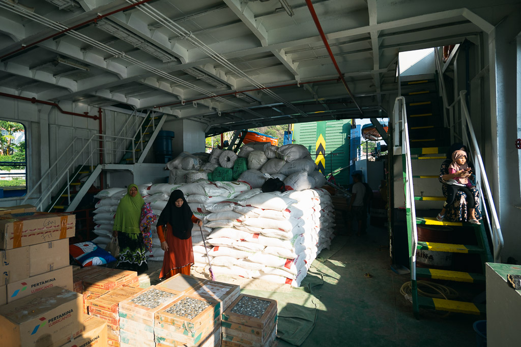 A bustling interior shot of a ferry shows stacks of white sacks and other cargo