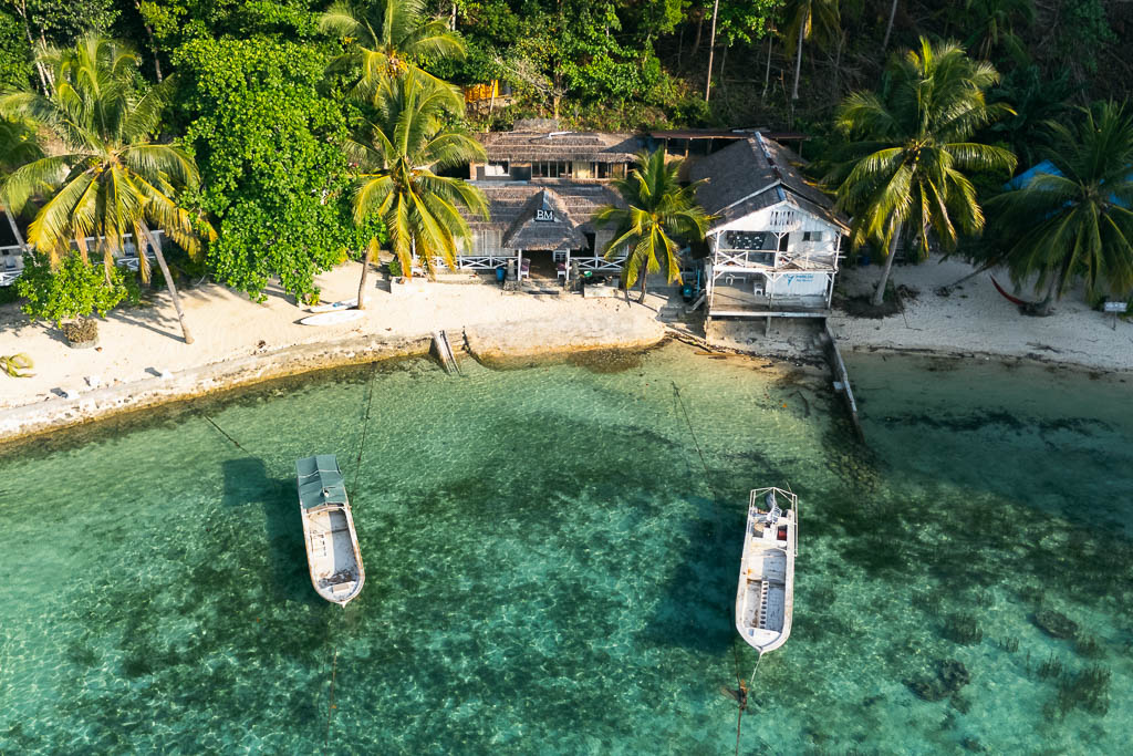 Aerial view of the Togean Islands shwoing a sandy beach with anchored boats, and tropical resort buildings