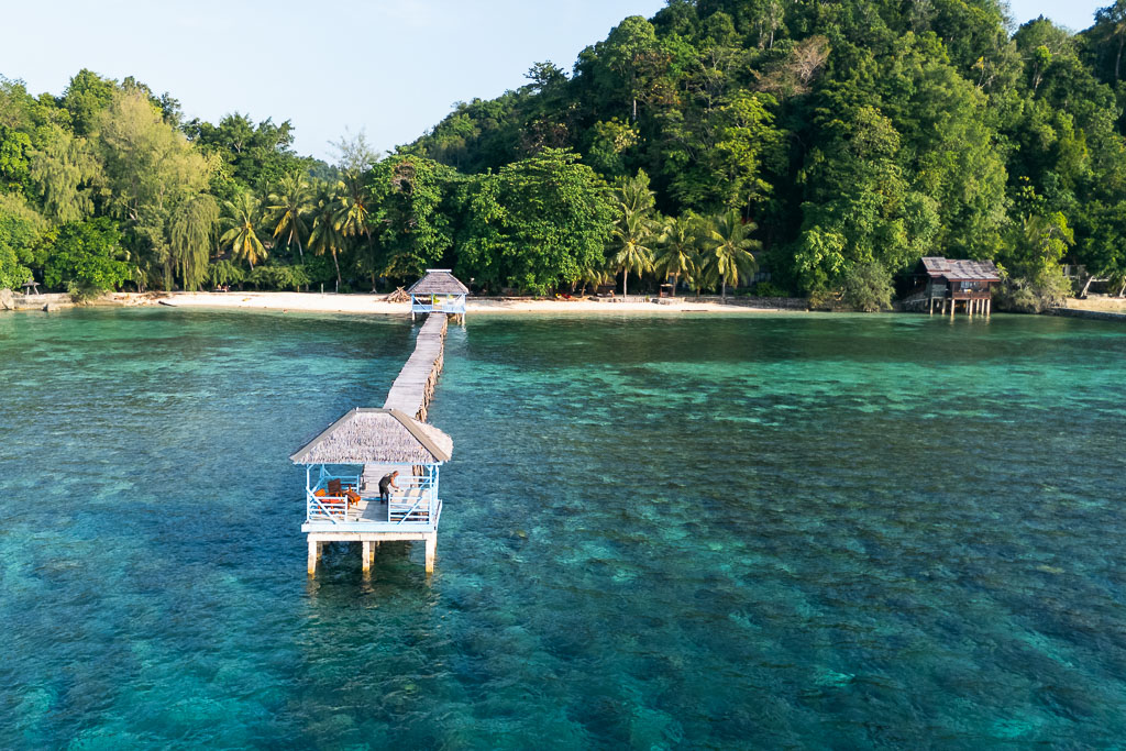Togean Islands pier with thatched huts, turquoise water, white sandy beach, and lush palm forest