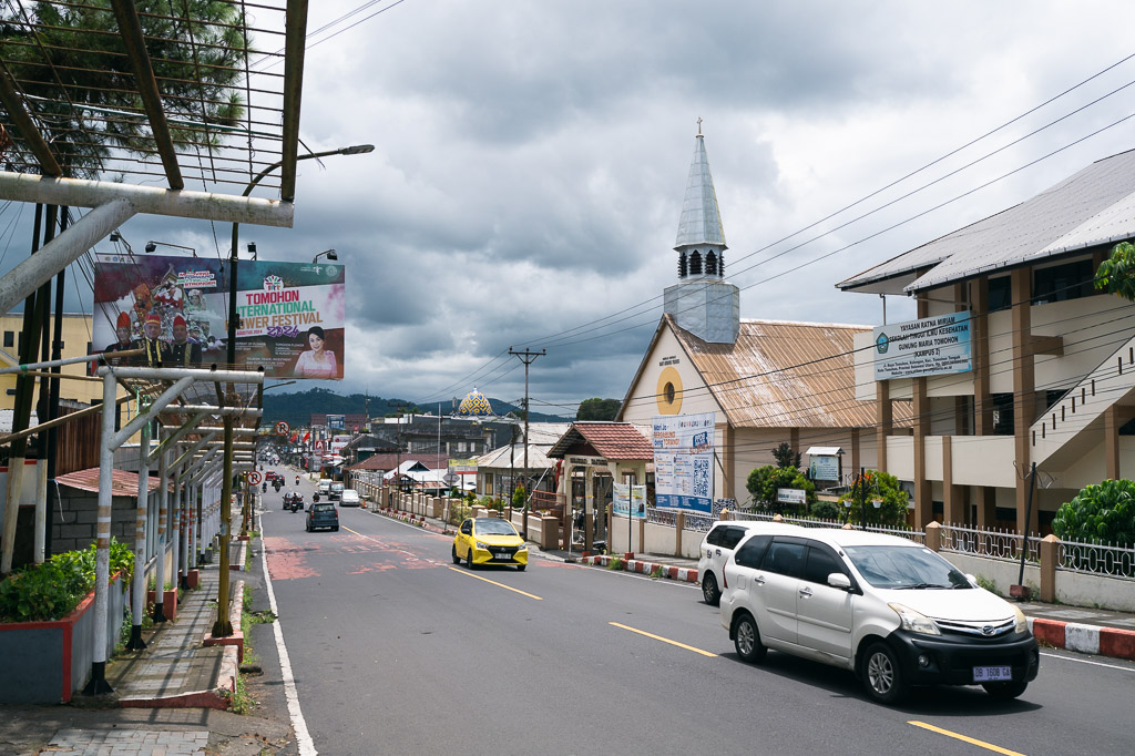 Street view in Tomohon with cars, a church, and a billboard for the Flower Festival