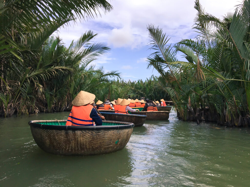 Tourists wearing life jackets and conical hats ride traditional round basket boats through a the Vietnamese coconut forest waterway